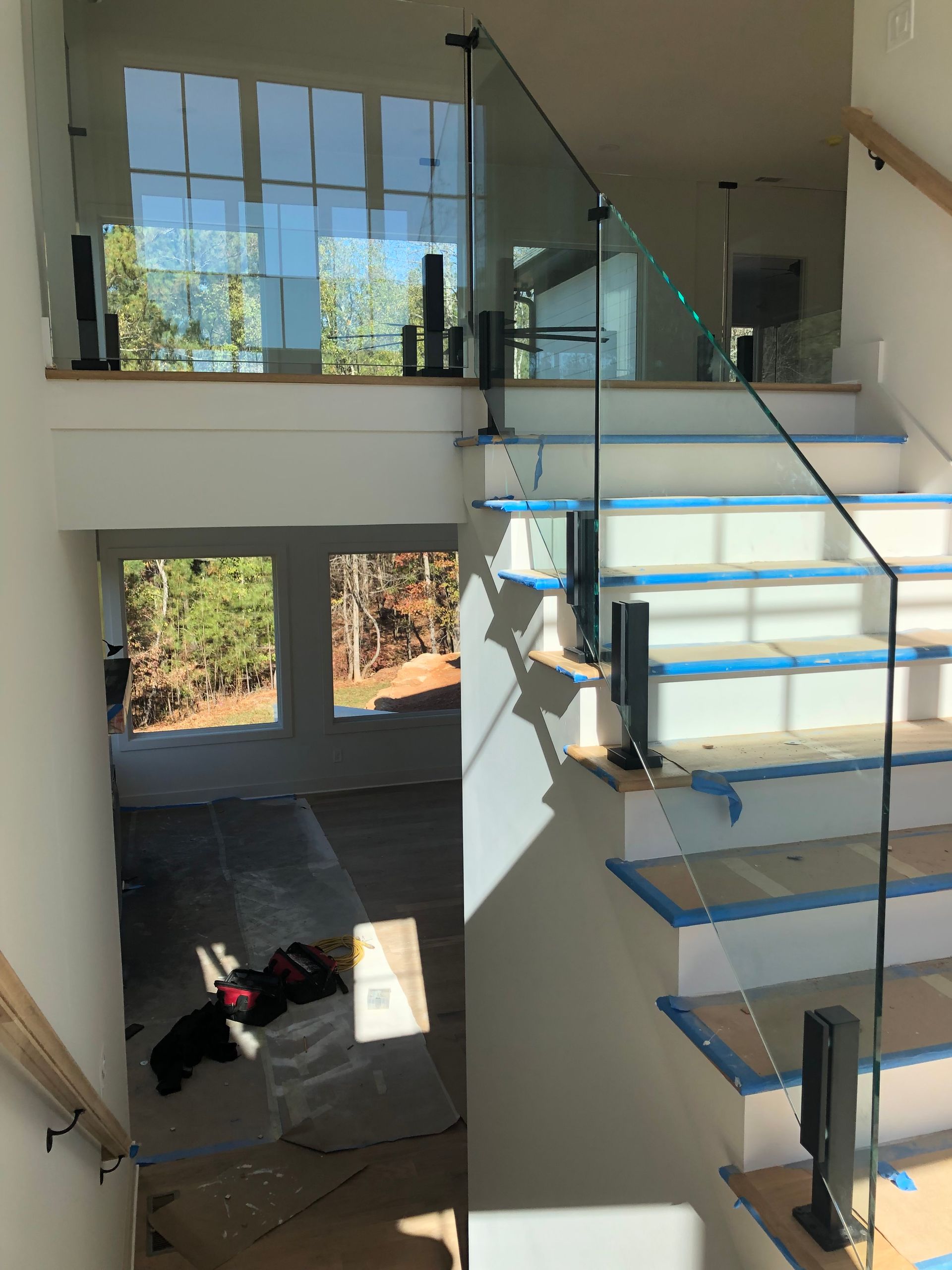 Modern stairway with glass railing overlooking a bright living room and large windows