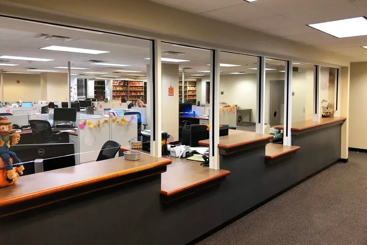 Library service desk with multiple windows, looking into an office area with cubicles and computers.