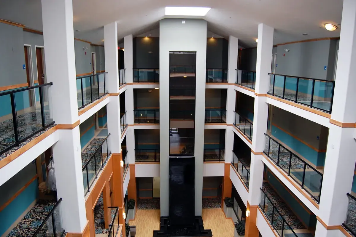 Multi-story interior hotel atrium with open balconies, a central elevator, and a skylight.