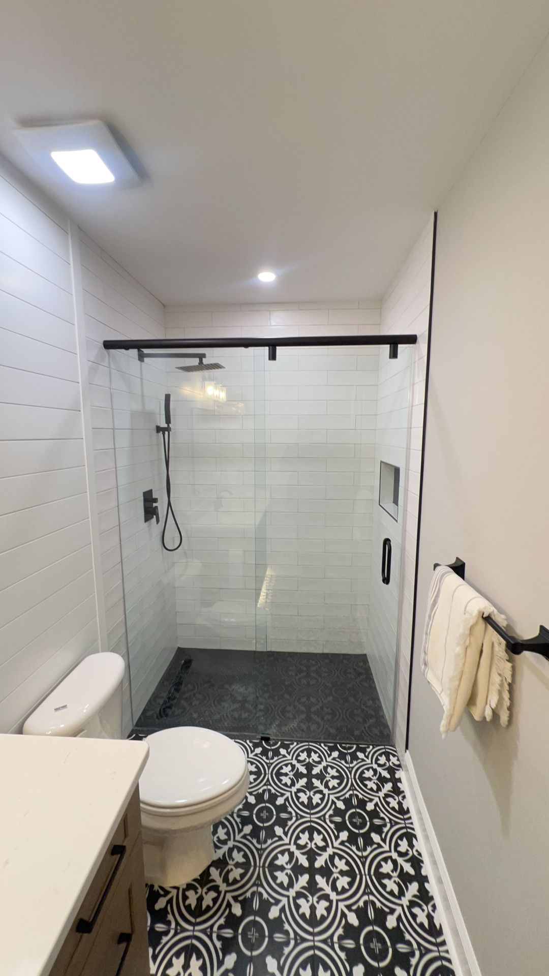 Modern bathroom with walk-in shower, patterned black-and-white floor tiles, and beige towels.