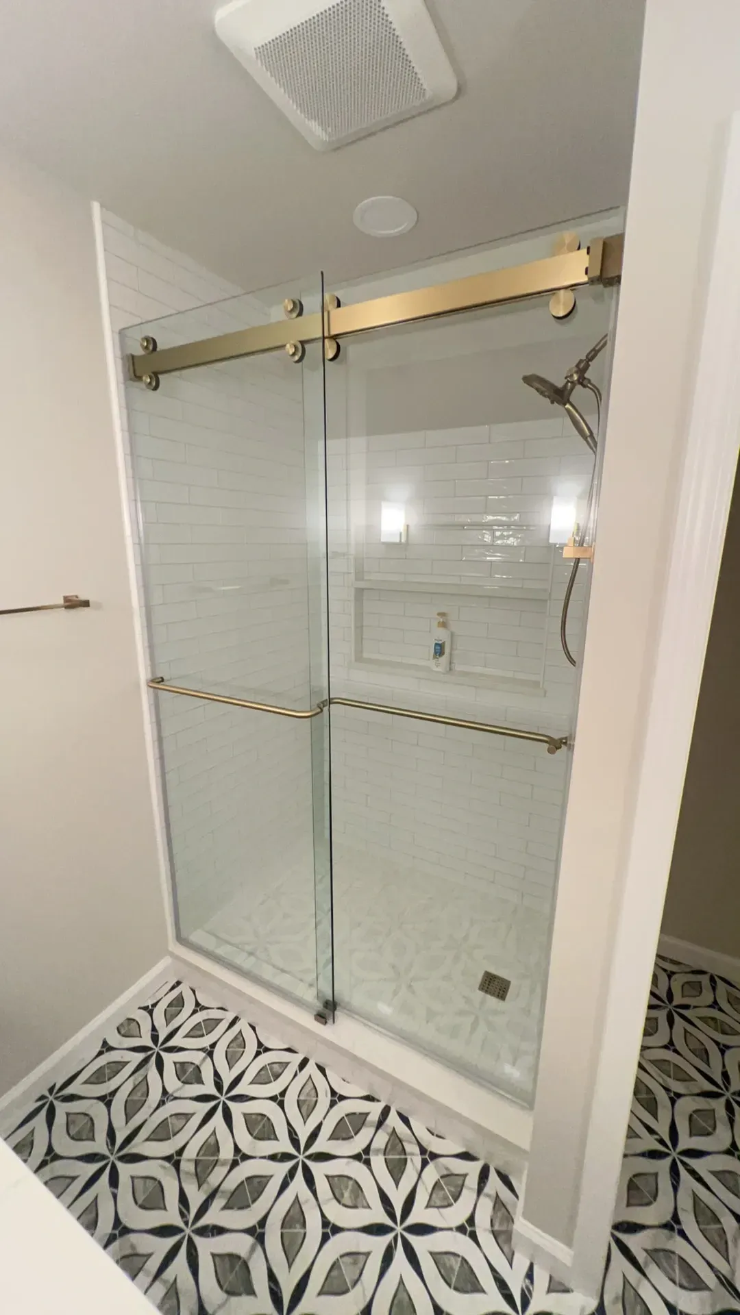 Bathroom with gold-framed glass shower doors, patterned floor tiles, and white walls.