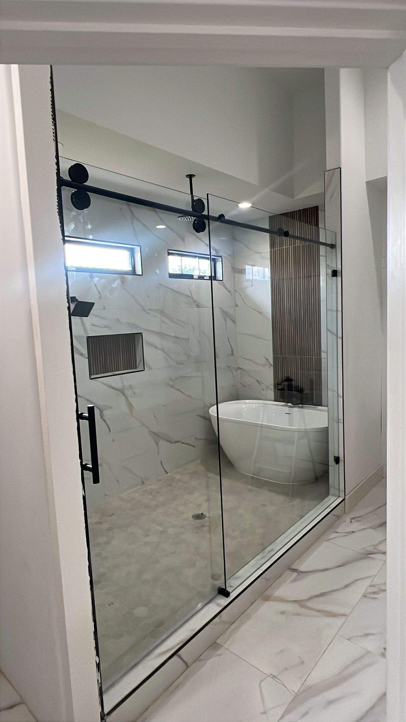 Modern bathroom with a glass shower enclosure, white marble tile, and a bathtub in the corner