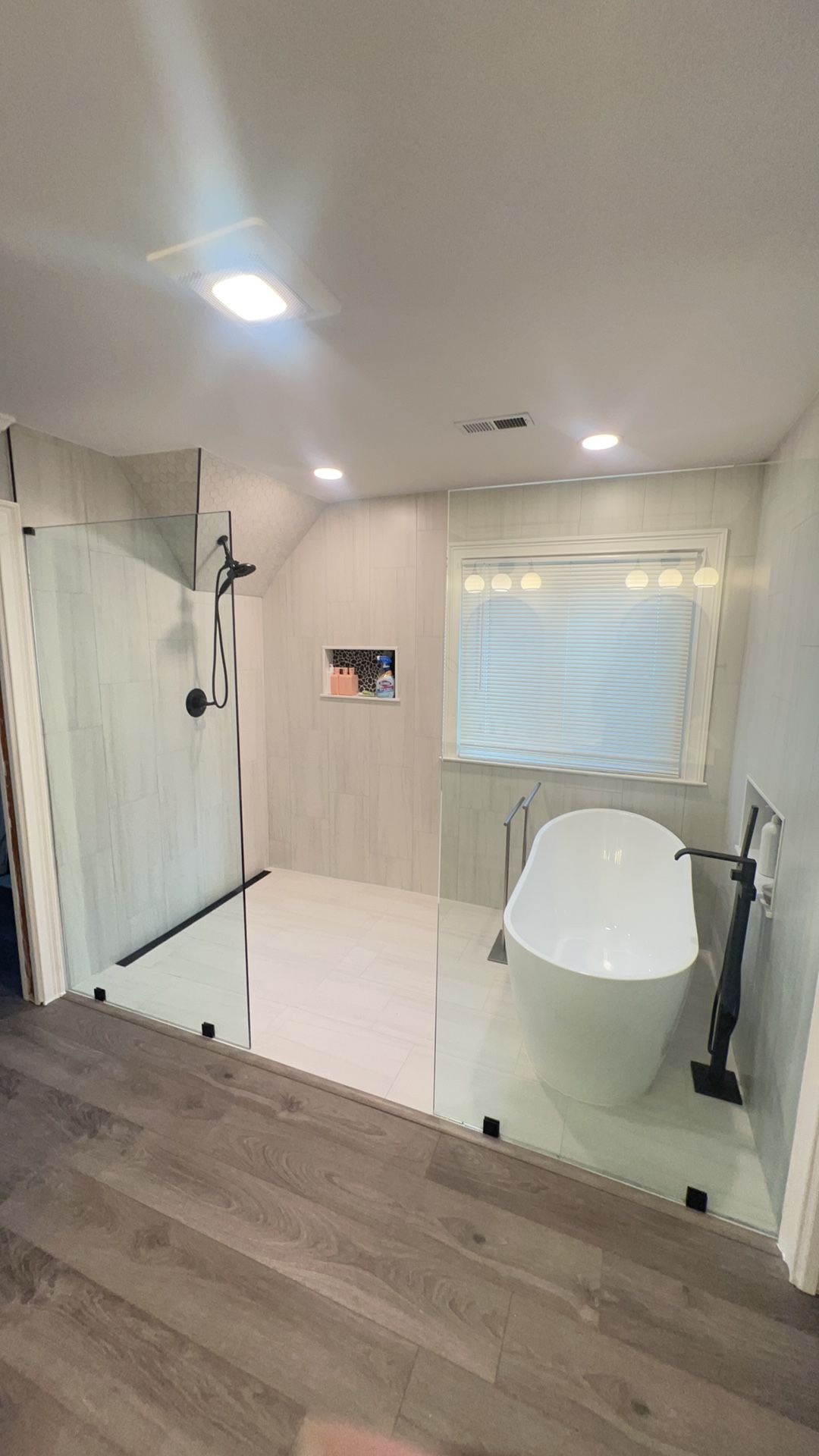 Modern bathroom with glass shower, white vanity, window blind, and wood flooring