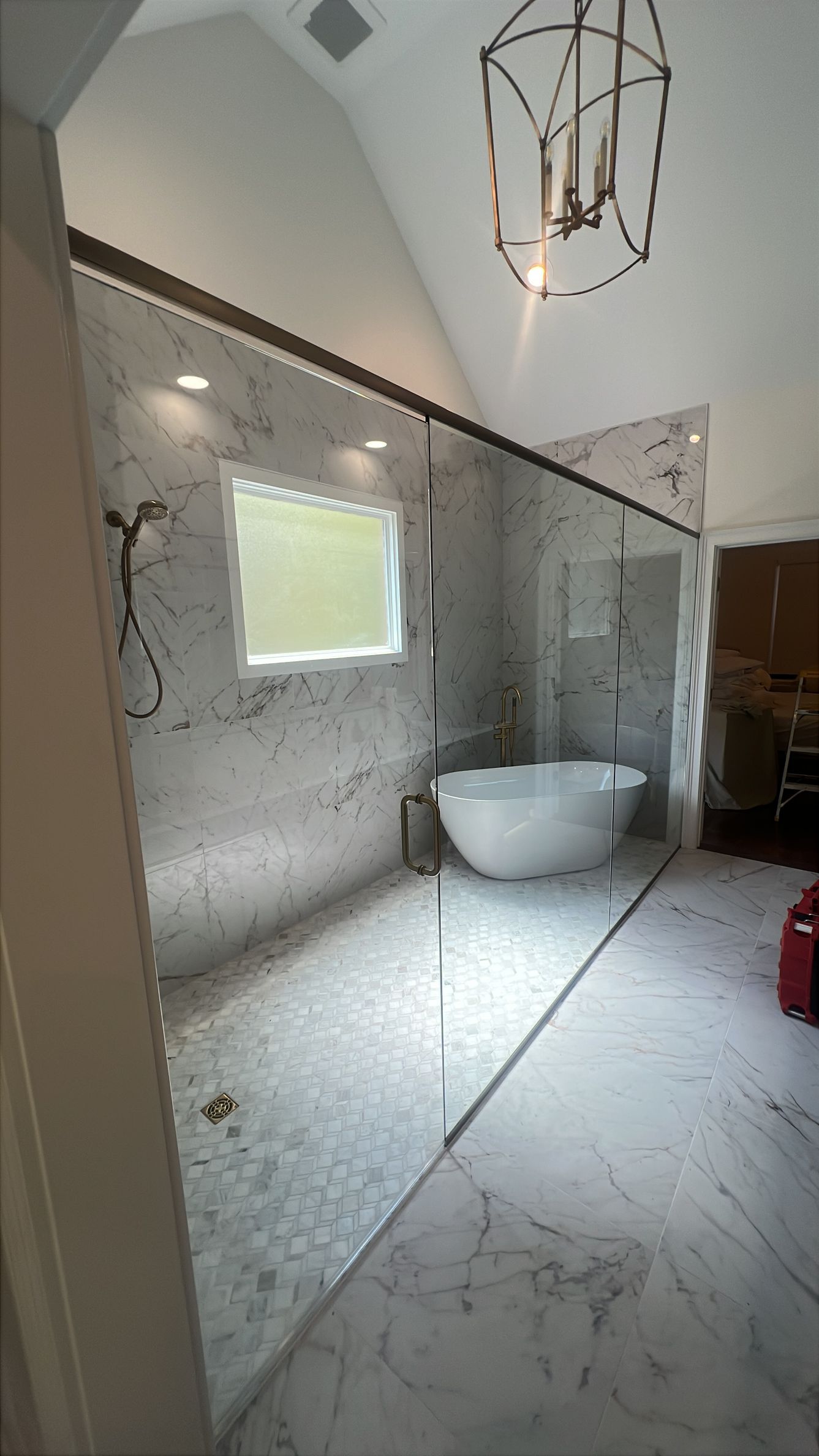 Modern bathroom with marble walls and floor, freestanding tub, window, and hanging pendant light