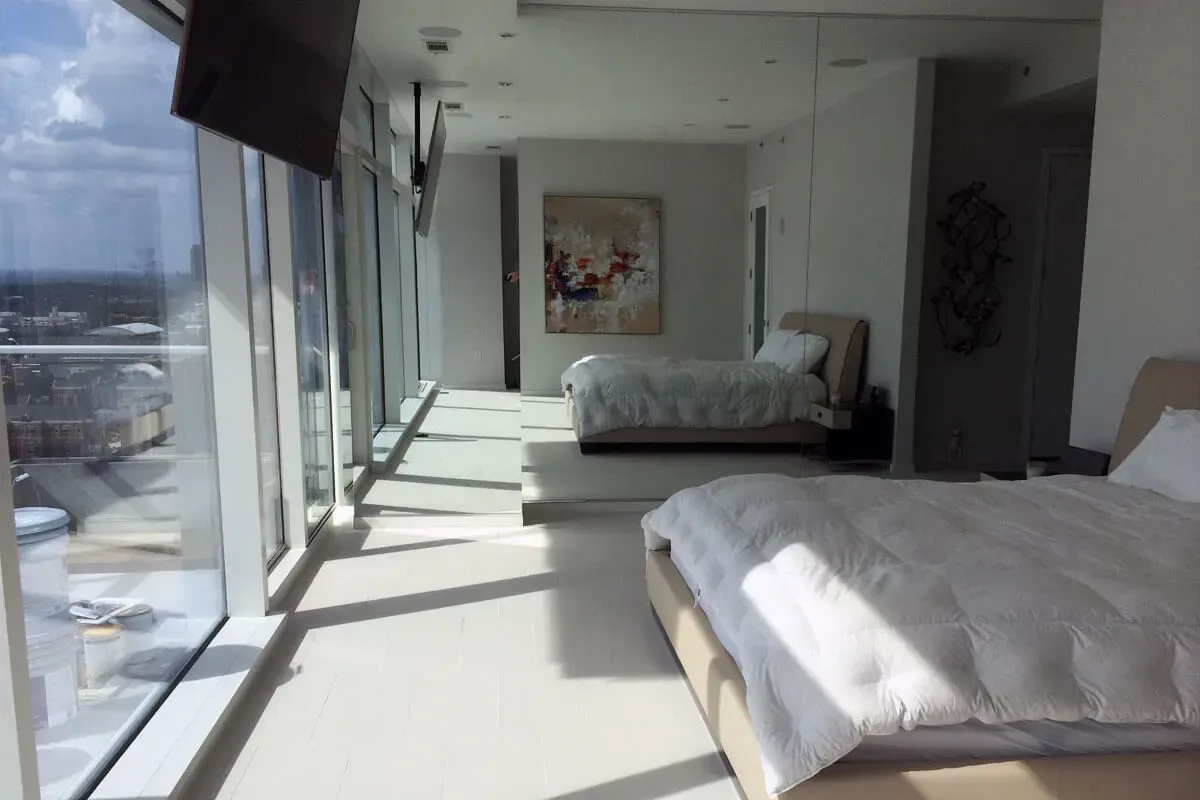 Bright, modern bedroom with large windows overlooking a city. Two beds with white linens.