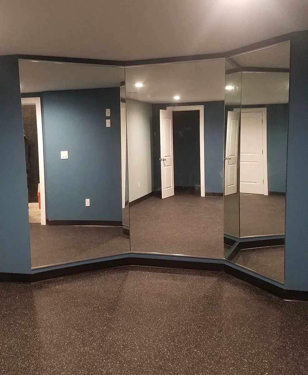 Mirrored wall in a room with blue walls, two white doors, and dark flooring.