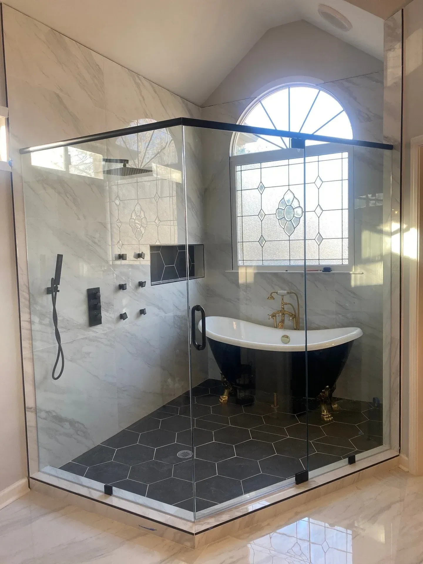 Spacious bathroom with glass shower, black tub, marble walls, and black floor tiles.