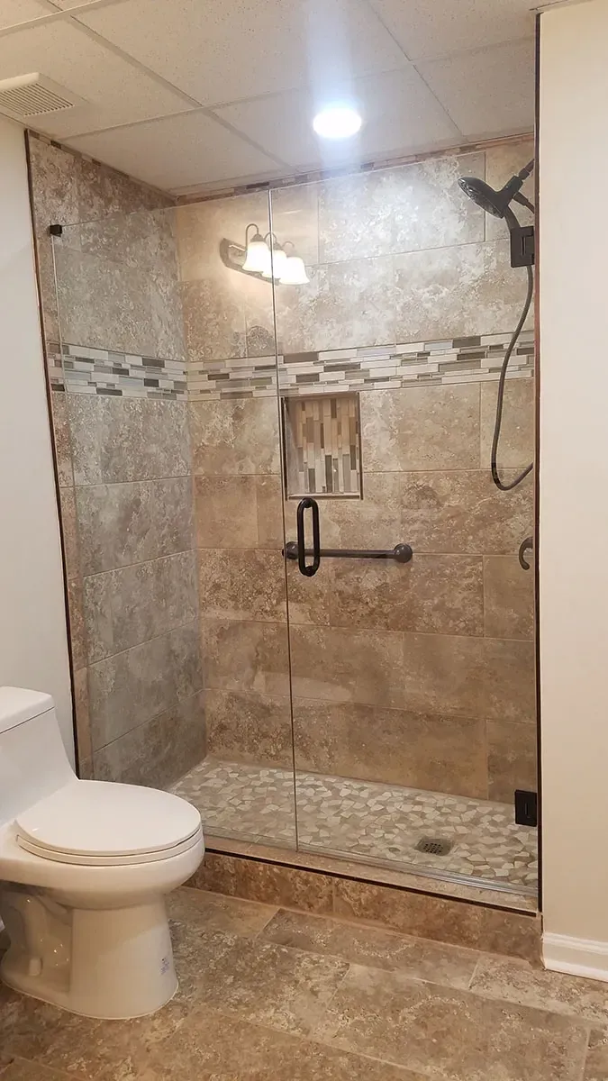 Bathroom with tiled shower, glass door, dark fixtures, and a white toilet.