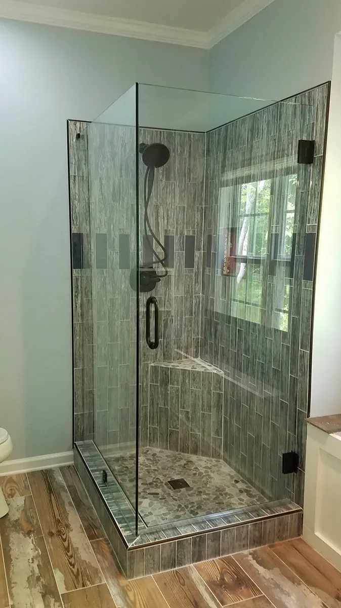 Glass shower with textured gray tile walls, dark fixtures, and a wooden floor.