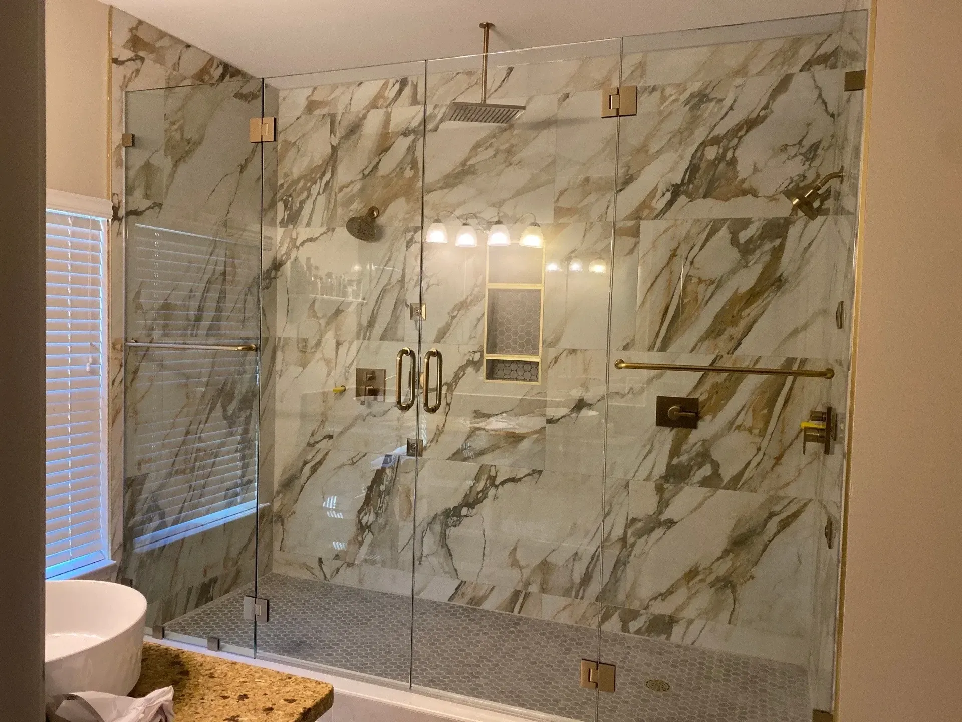 Glass shower enclosure with gold hardware, marble tile, and two doors.