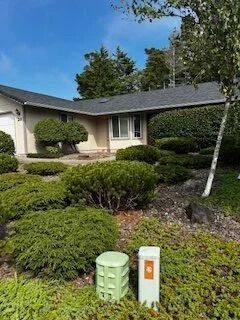 Single-story house with manicured shrubs and a green utility marker in the front yard.