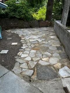 Stone patio with irregular flagstones, bordered by a low wall and greenery.