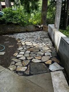 Stone-paved garden walkway beside a concrete wall and greenery