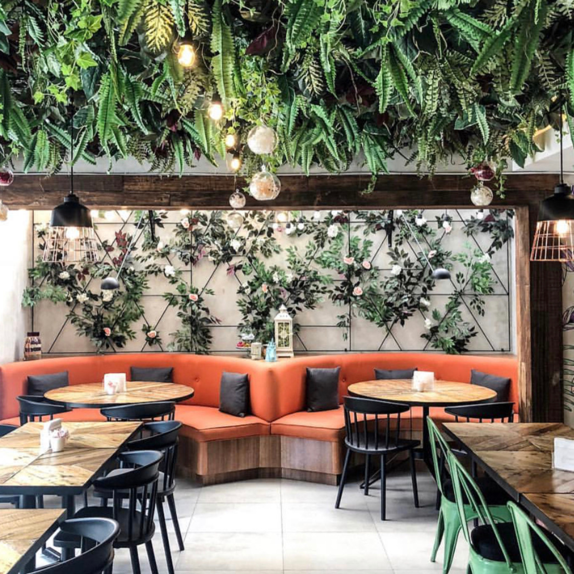 Restaurant interior with orange booths, black chairs, and a floral wall and ceiling decor.
