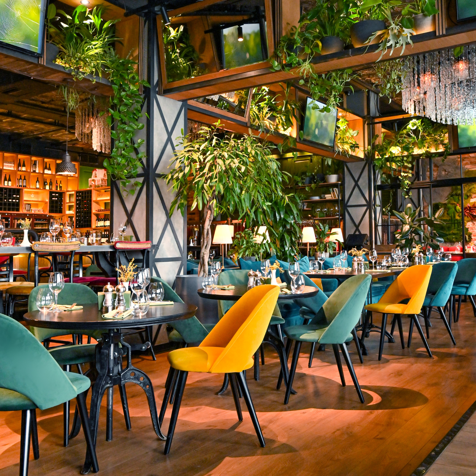A modern restaurant interior with green and yellow chairs, lush plants, and stylish decor.