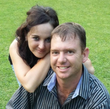 Woman with arm around man, both smiling outdoors.