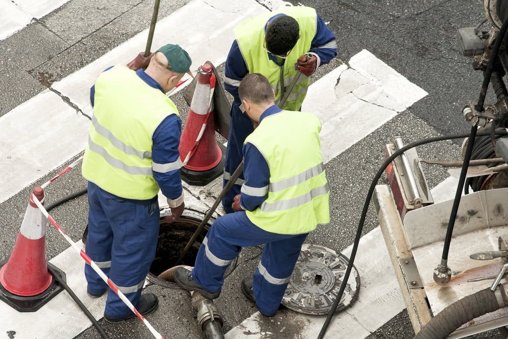 A Group Of Men Are Working On A Manhole Cover — DAVMAC Plumbing in Wauchope, NSW
