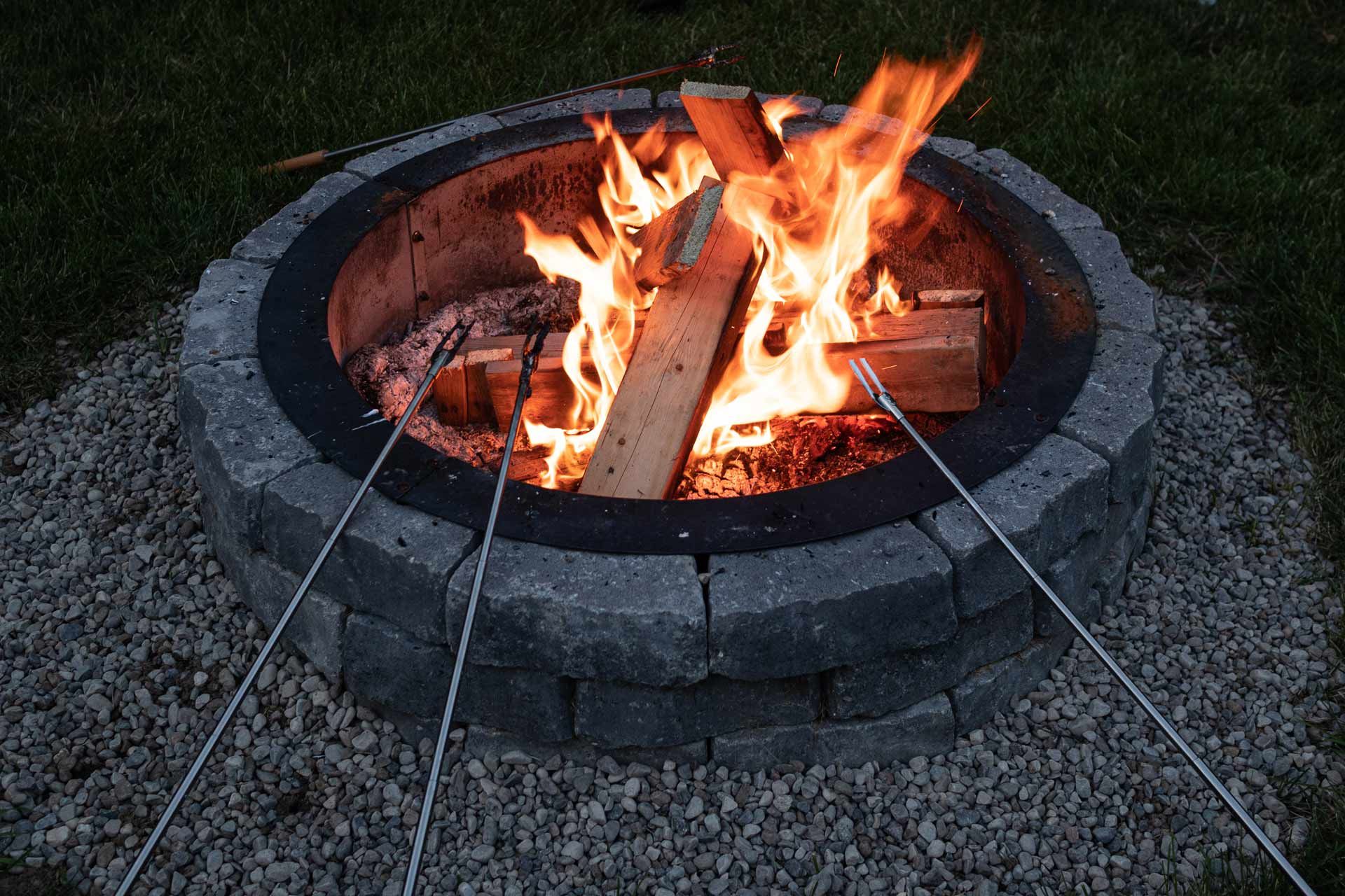 Fire pit with a blazing fire, surrounded by gray stone and gravel.