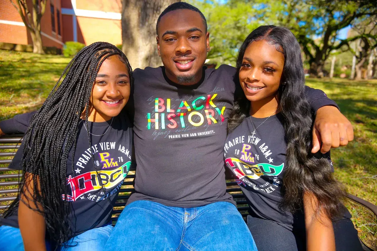 A man and two girls are sitting on a bench wearing black history shirts.