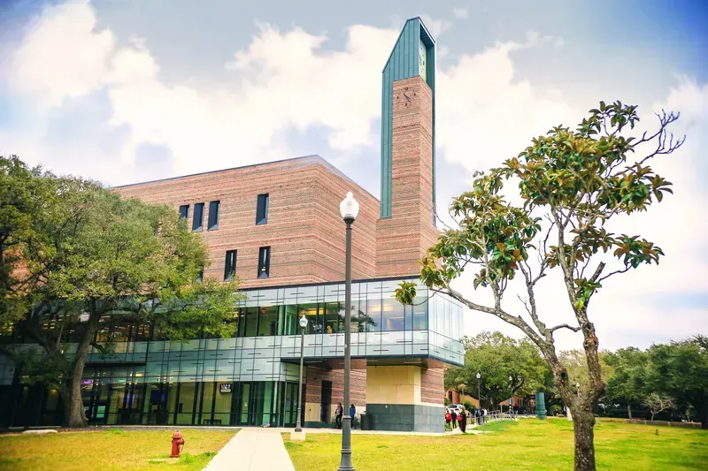 A large brick building with a clock tower is surrounded by trees and grass.