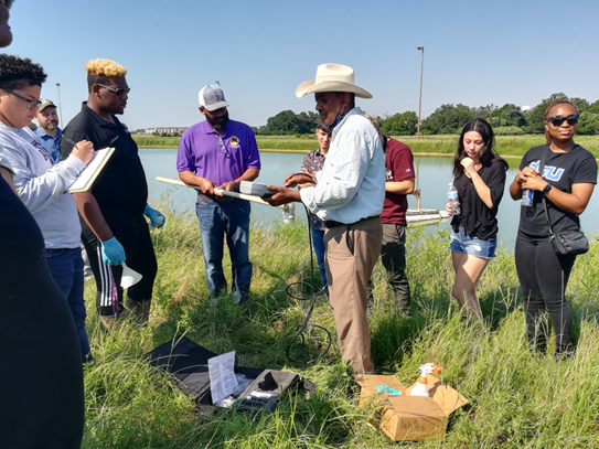 A group of people are standing in a field near a body of water.