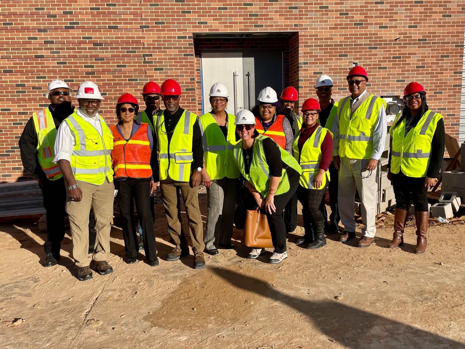 A group of construction workers are posing for a picture in front of a brick building.