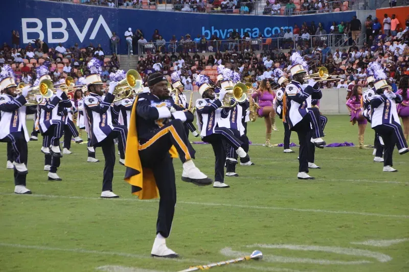 A marching band is performing on a field in front of a bbva sign