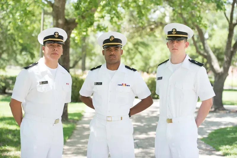 Three men in military uniforms are standing next to each other in a park.