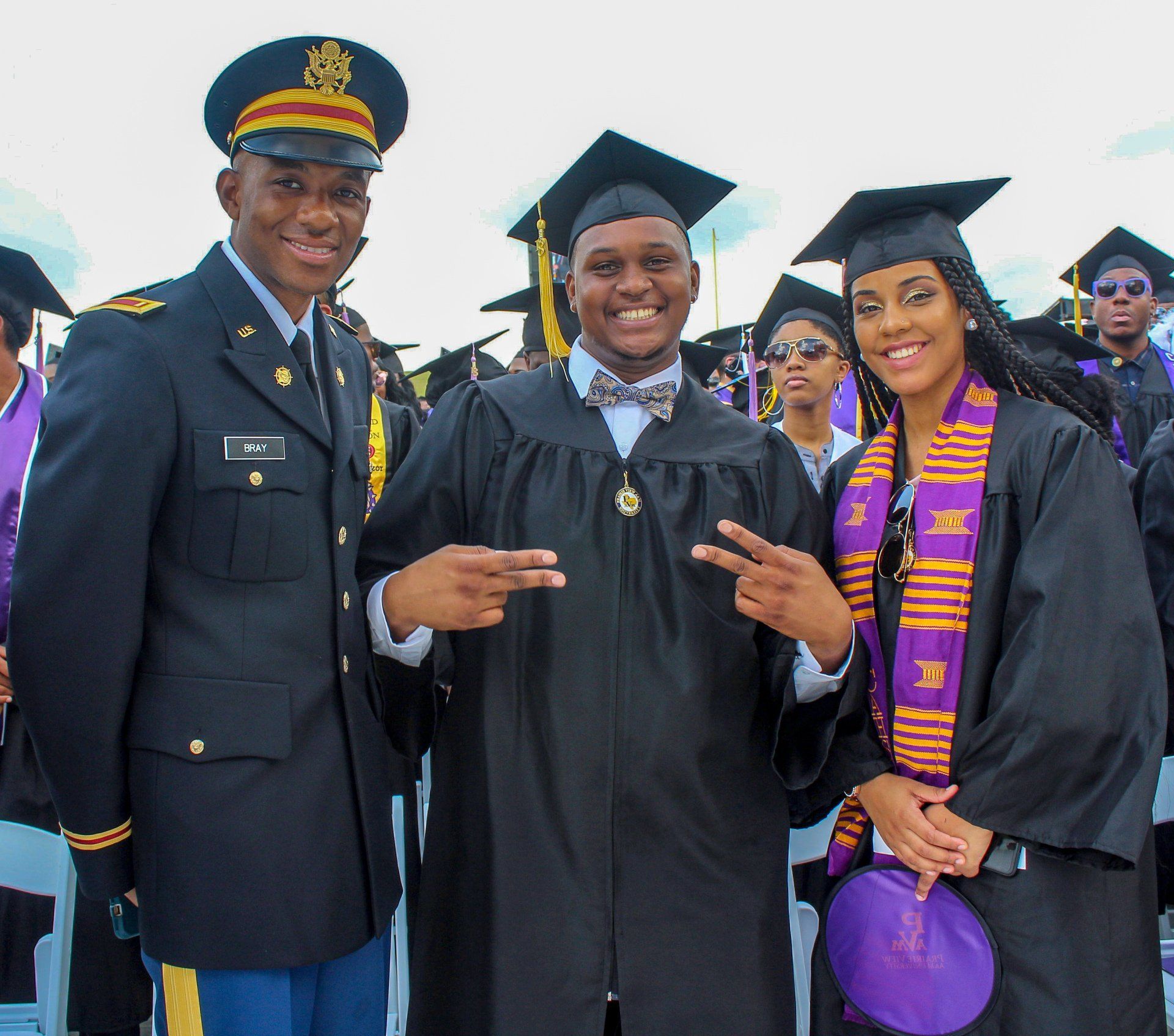 A man in a military uniform stands next to two graduates