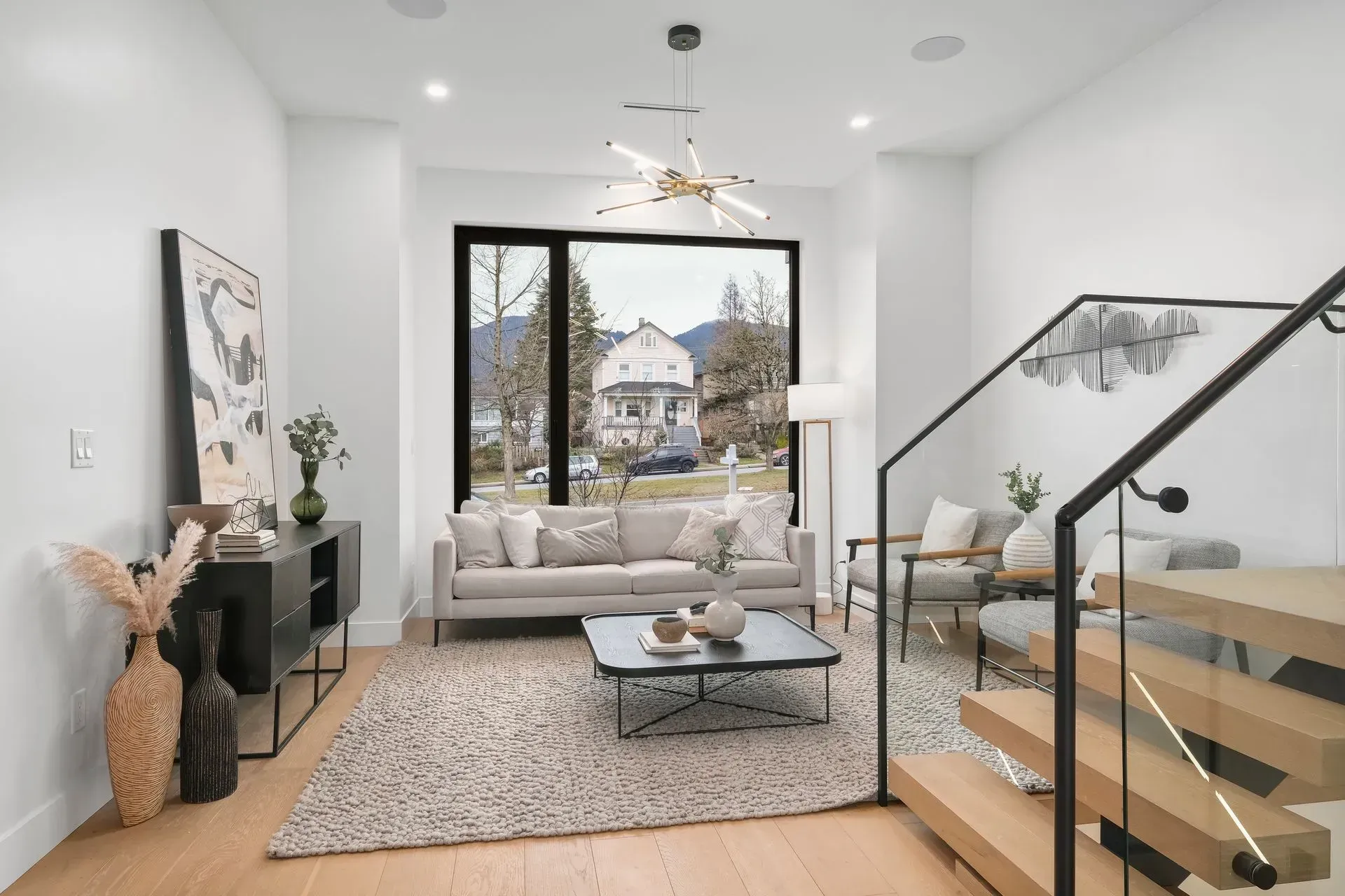 Modern living room with neutral colors, large window, and floating staircase.