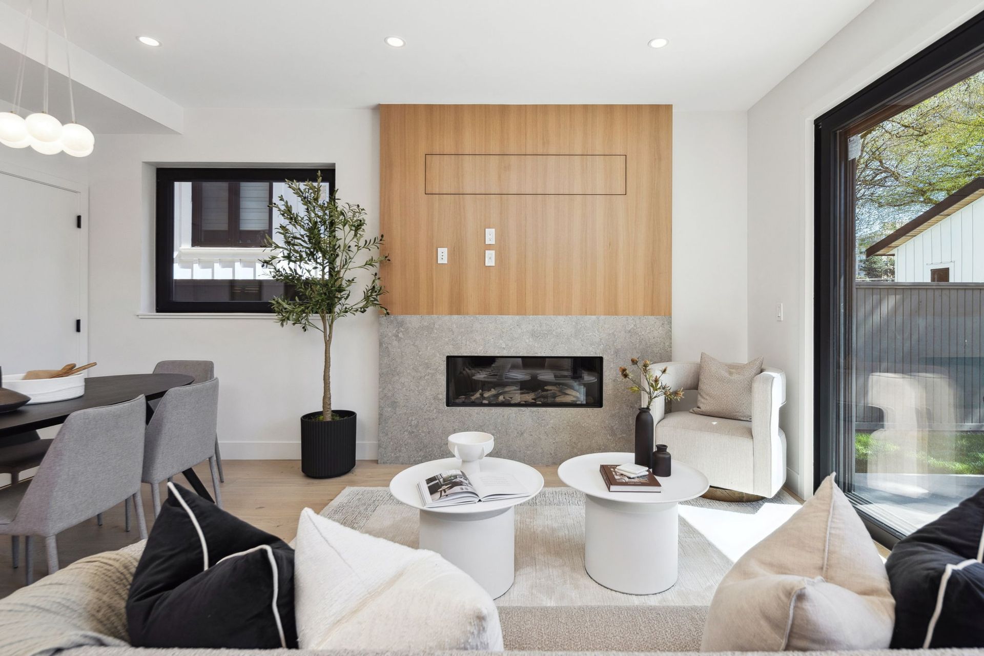 Modern living room with fireplace, wood paneling, white and gray decor, and outdoor view.