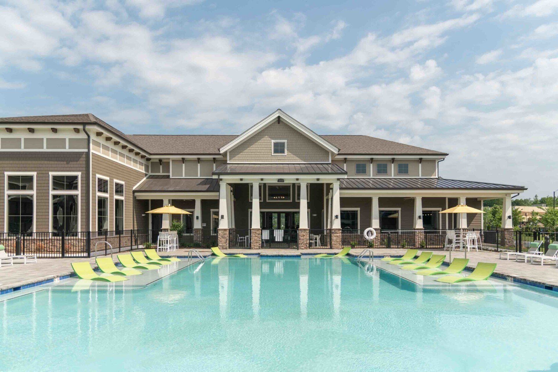 A sunny, modern clubhouse with a swimming pool in the foreground, featuring lime green lounge chairs at the water's edge at Silver Collection at Celebrate apartment community in Fredericksburg, VA.