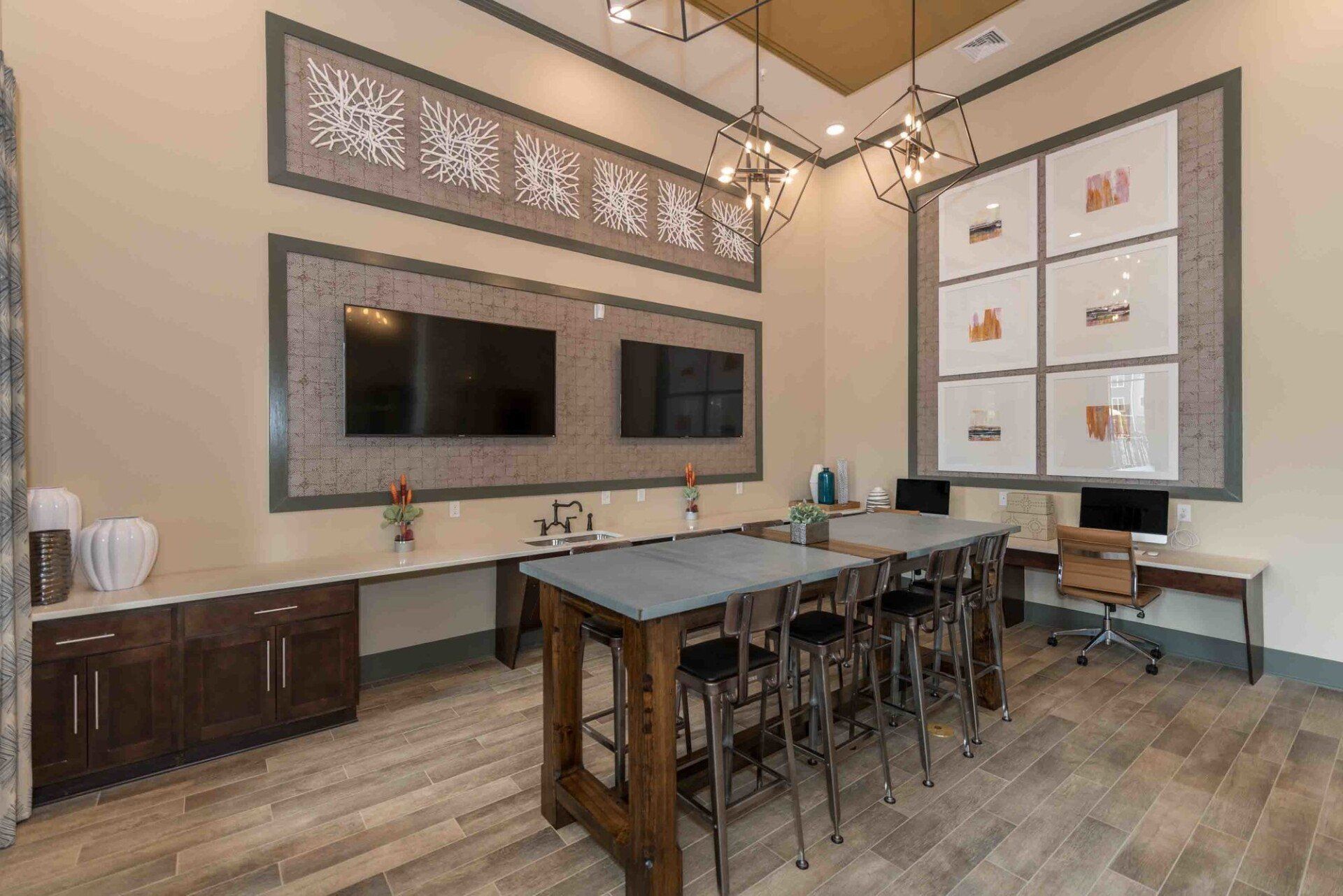 A community room with a long central table, wall-mounted TVs, a desk area with computers, and decorative wall panels at Silver Collection at Celebrate apartment community in Fredericksburg, VA.