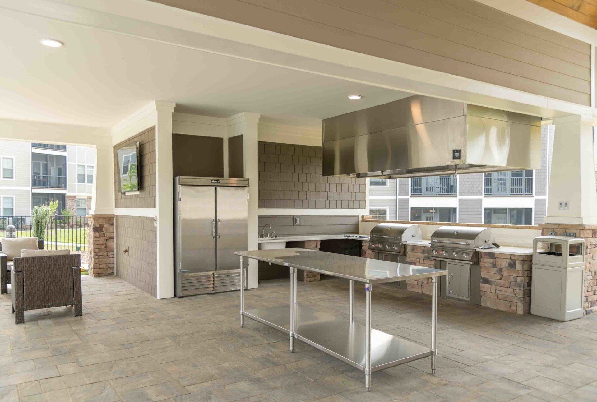 An outdoor kitchen with stainless steel appliances, a prep table, and a grill under a covered patio at Silver Collection at Celebrate apartment community in Fredericksburg, VA.