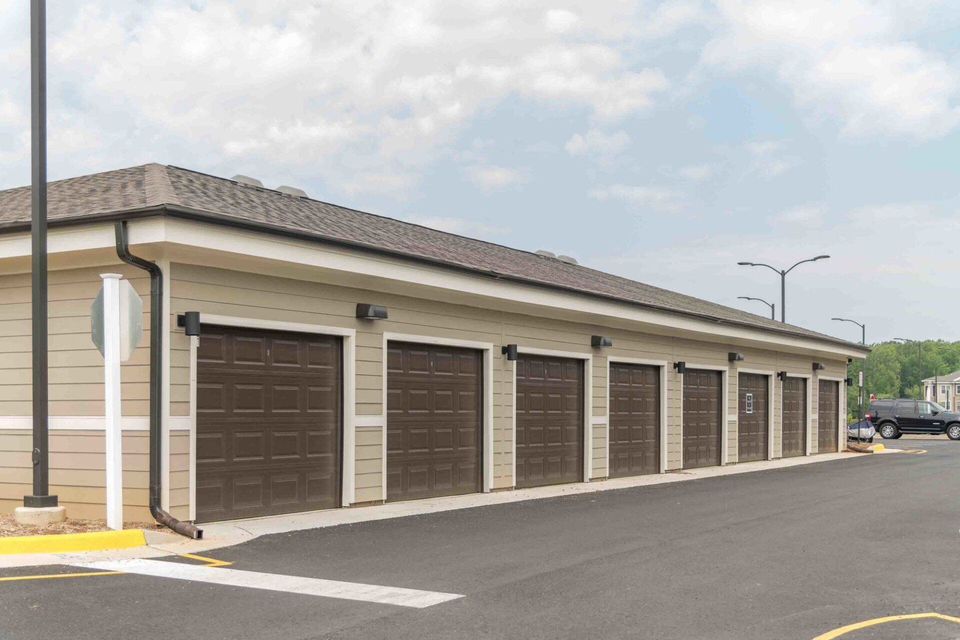 A tan, single-story building with a row of multiple brown garage doors, situated in an outdoor parking lot at Silver Collection at Celebrate apartment community in Fredericksburg, VA.