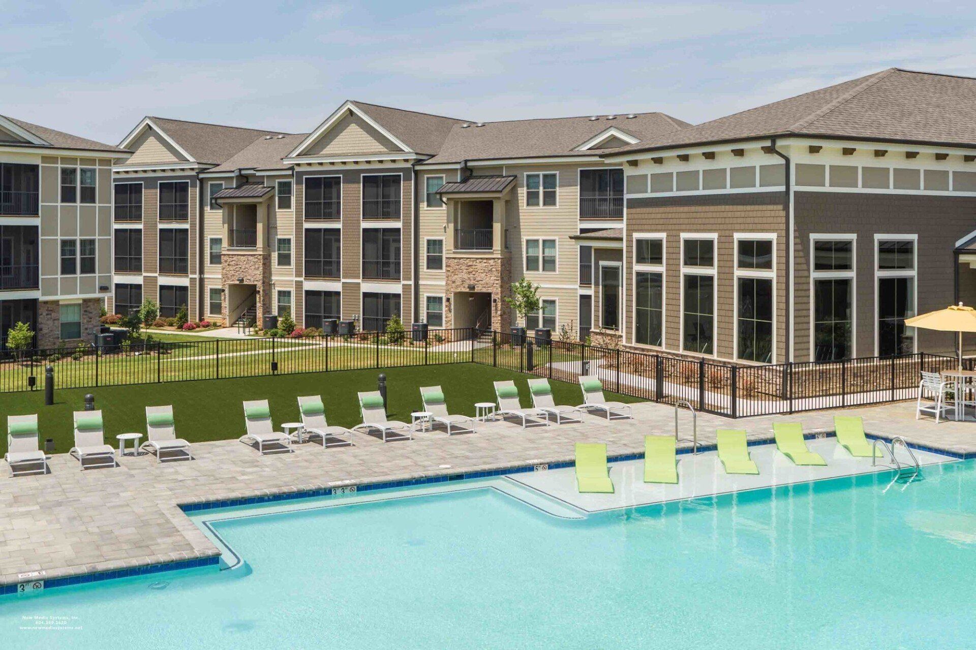 An outdoor swimming pool surrounded by a patio with lime green lounge chairs in front of an apartment complex at Silver Collection at Celebrate apartment community in Fredericksburg, VA.