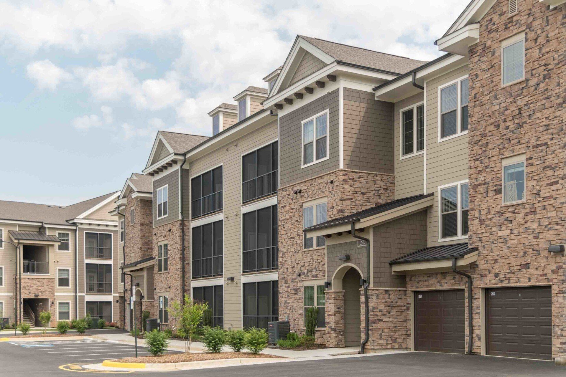 A multi-story apartment building with beige siding, brick accents, dark-framed windows, and ground-level garage doors at Silver Collection at Celebrate apartment community in Fredericksburg, VA.