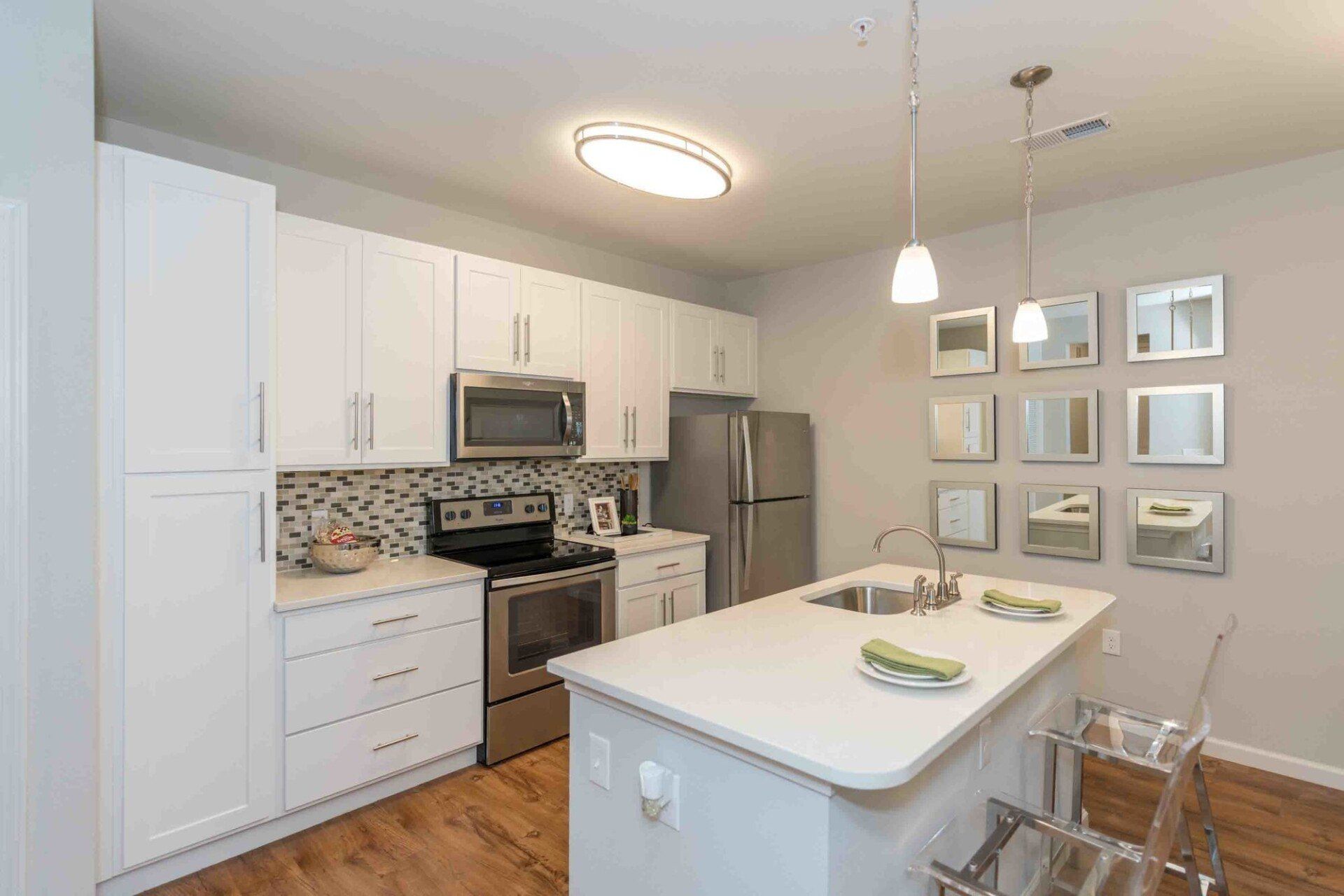 A modern kitchen featuring white cabinets, stainless steel appliances, a white island, and a decorative wall of mirrors at Silver Collection at Celebrate apartment community in Fredericksburg, VA.