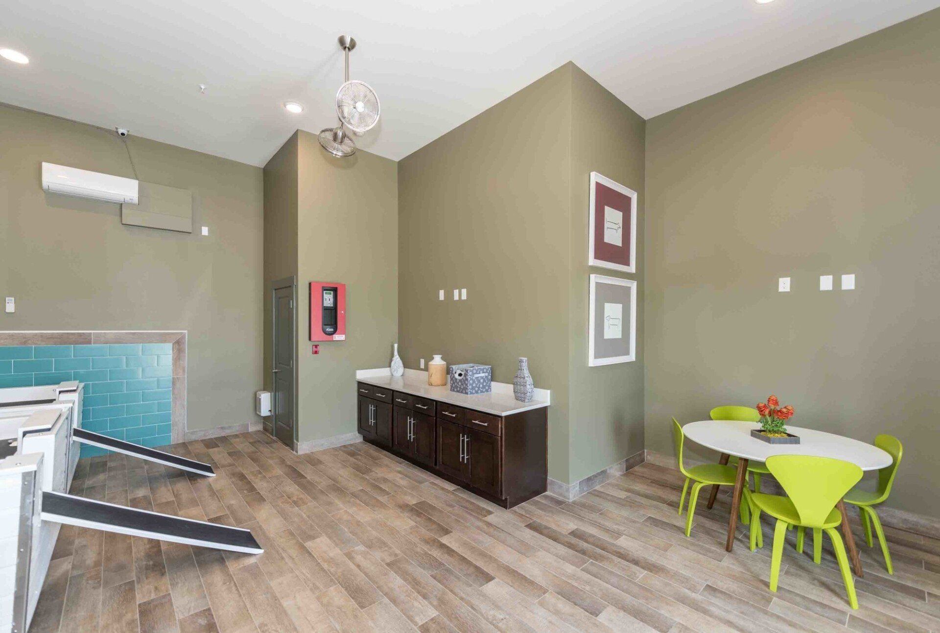 A room with treadmills, a dark wooden console, and a white table with four lime-green chairs on a wood-look floor at Silver Collection at Celebrate apartment community in Fredericksburg, VA.
