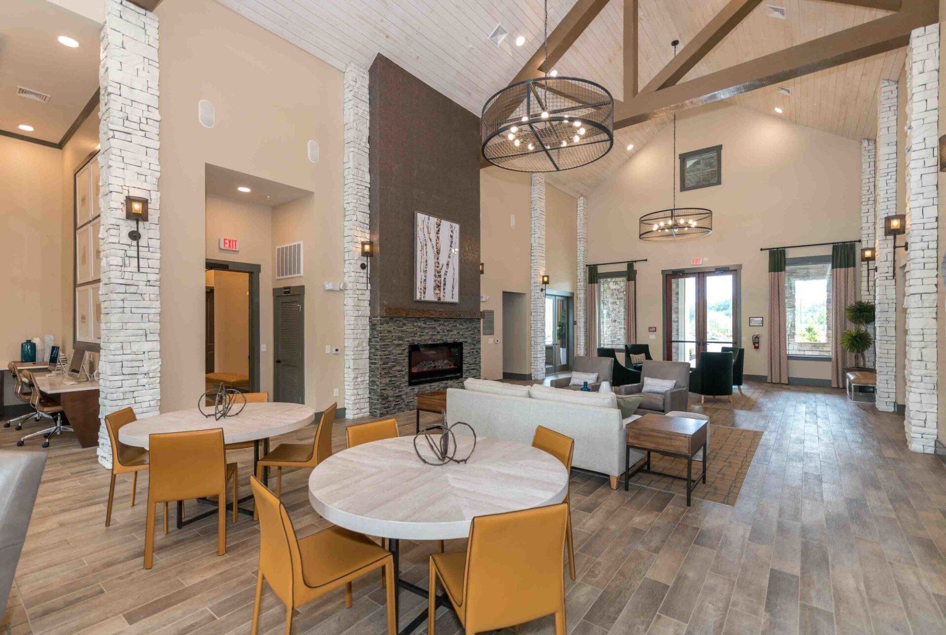 A spacious, modern lounge area with tables, chairs, a fireplace. It has high ceilings and exposed wooden beams.