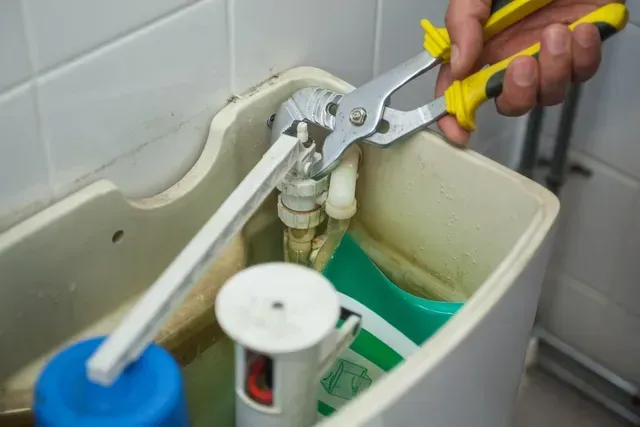 Hand using a wrench to repair a toilet's flushing mechanism in close-up view.