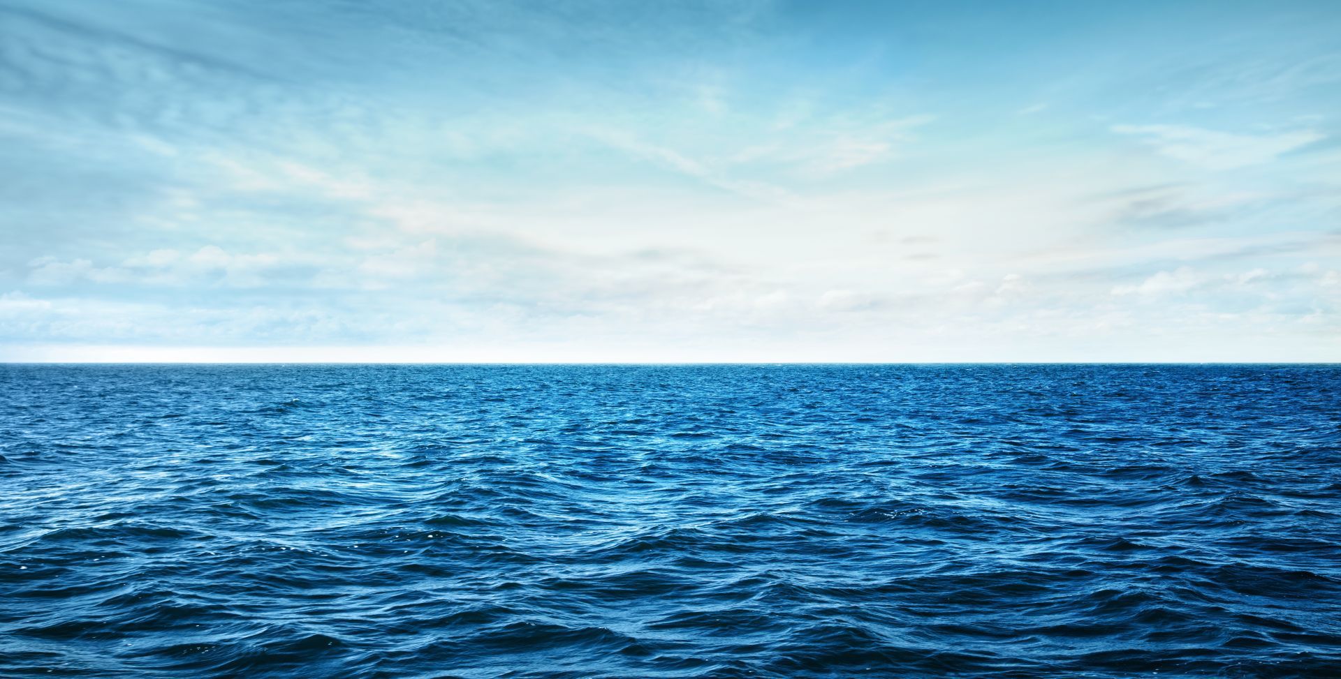 Vast blue ocean under a pale cloudy sky on the horizon