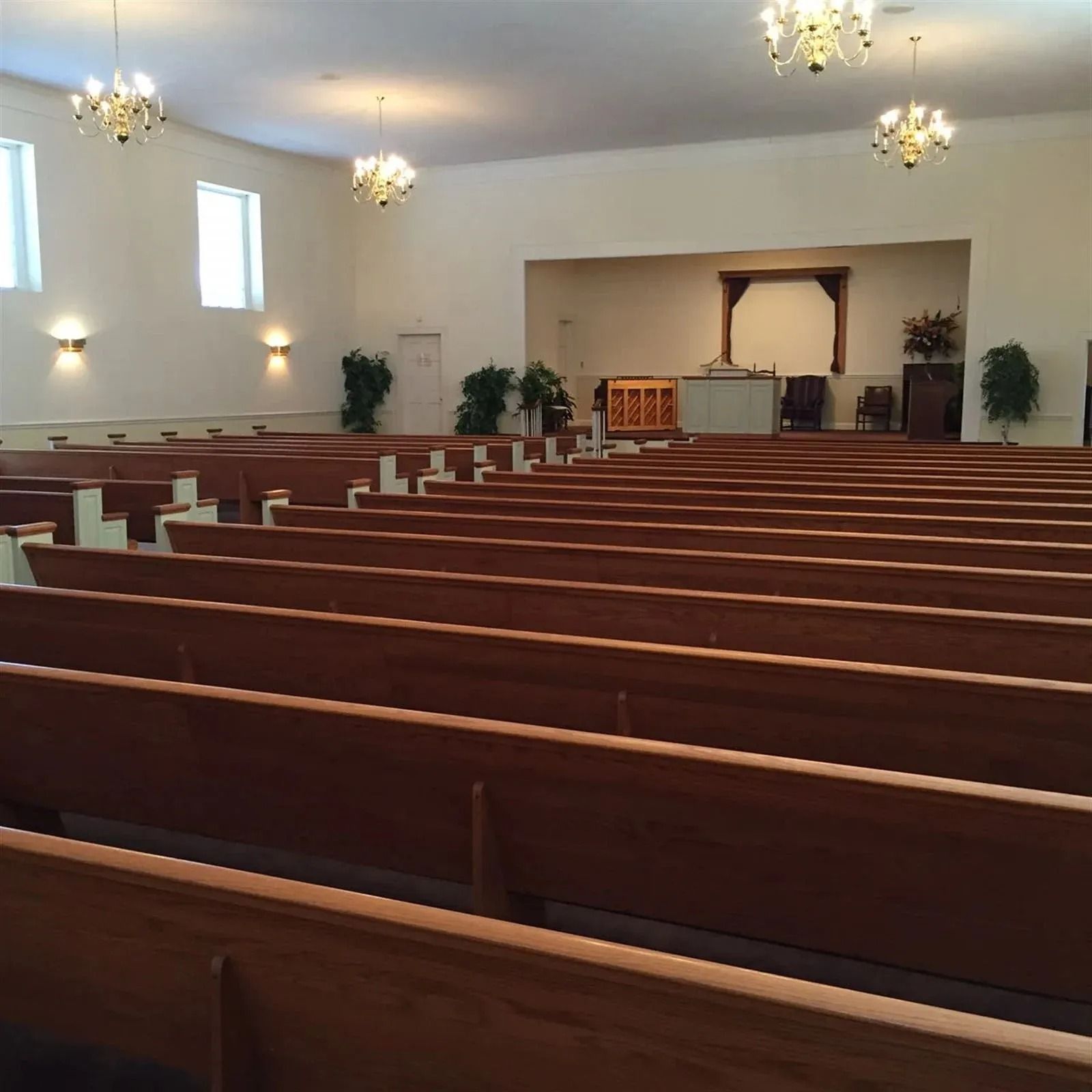 Empty church sanctuary with wooden pews facing a raised altar, chandeliers, and soft wall lights