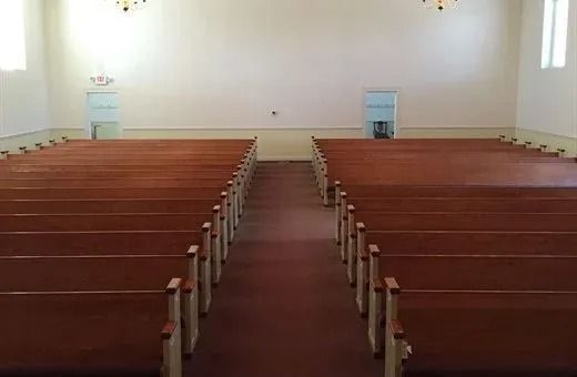 Empty church interior with wooden pews and a central aisle under white walls.