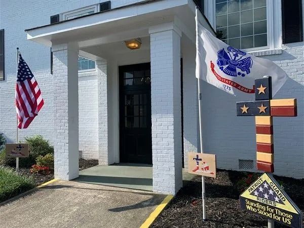 Front porch with American flags and a large decorative cross on a white house.