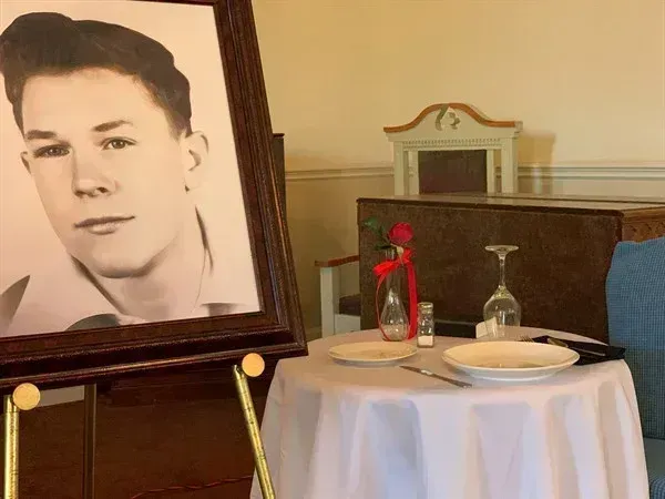 Framed black-and-white portrait beside a small memorial table with flowers, candles, and plates.