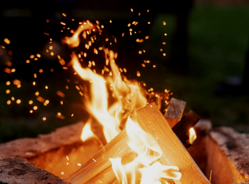 Close-up of a campfire with bright orange flames and glowing embers against a dark background