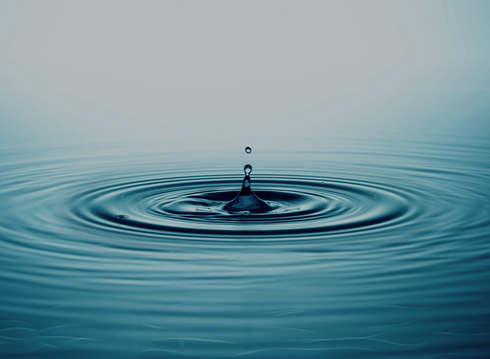 Water droplet creating concentric ripples on a calm blue surface