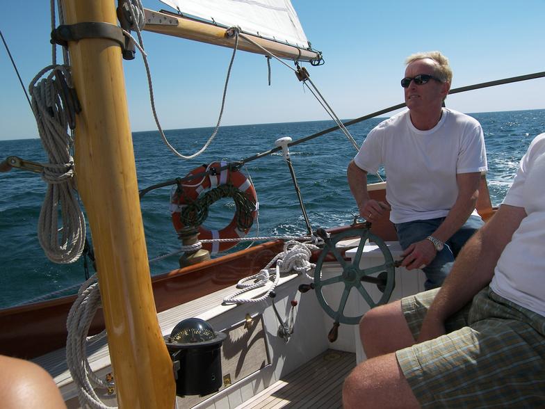 A man sits at the steering wheel of a sailboat