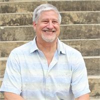 Smiling man in a light blue striped shirt seated on stone steps